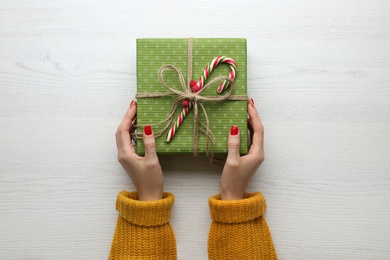 Woman holding Christmas gift box at white wooden table, top view