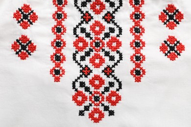 Photo of Beautiful red Ukrainian national embroidery on white fabric, top view