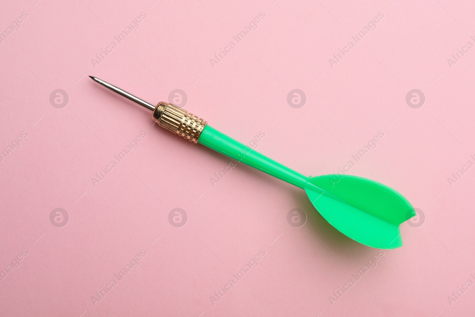 Photo of Green dart arrow on pink background, top view