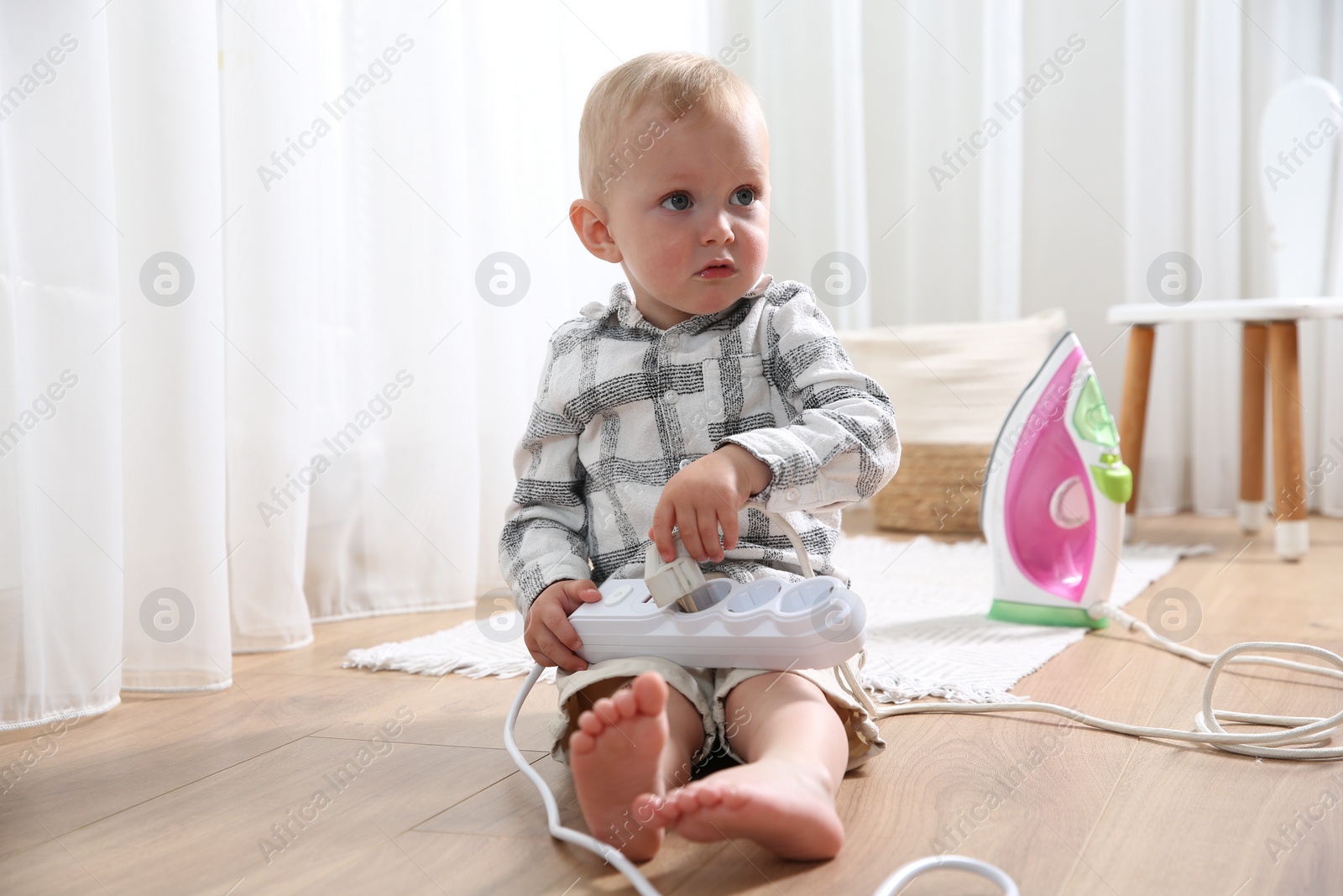 Photo of Little child playing with power strip and iron plug on floor at home. Dangerous situation