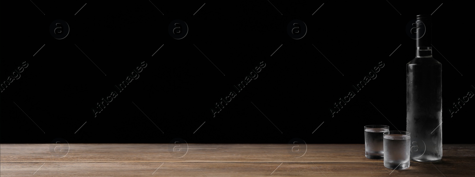 Image of Bottle of vodka and shot glasses on wooden table against black background, space for text. Banner design