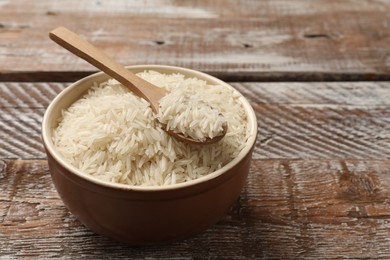 Photo of Raw basmati rice and spoon in bowl on wooden table, space for text