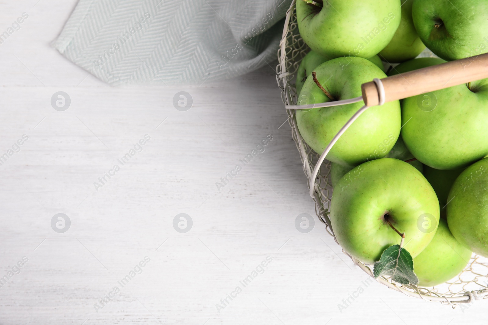 Photo of Metal basket of fresh ripe green apples on white wooden table, top view. Space for text