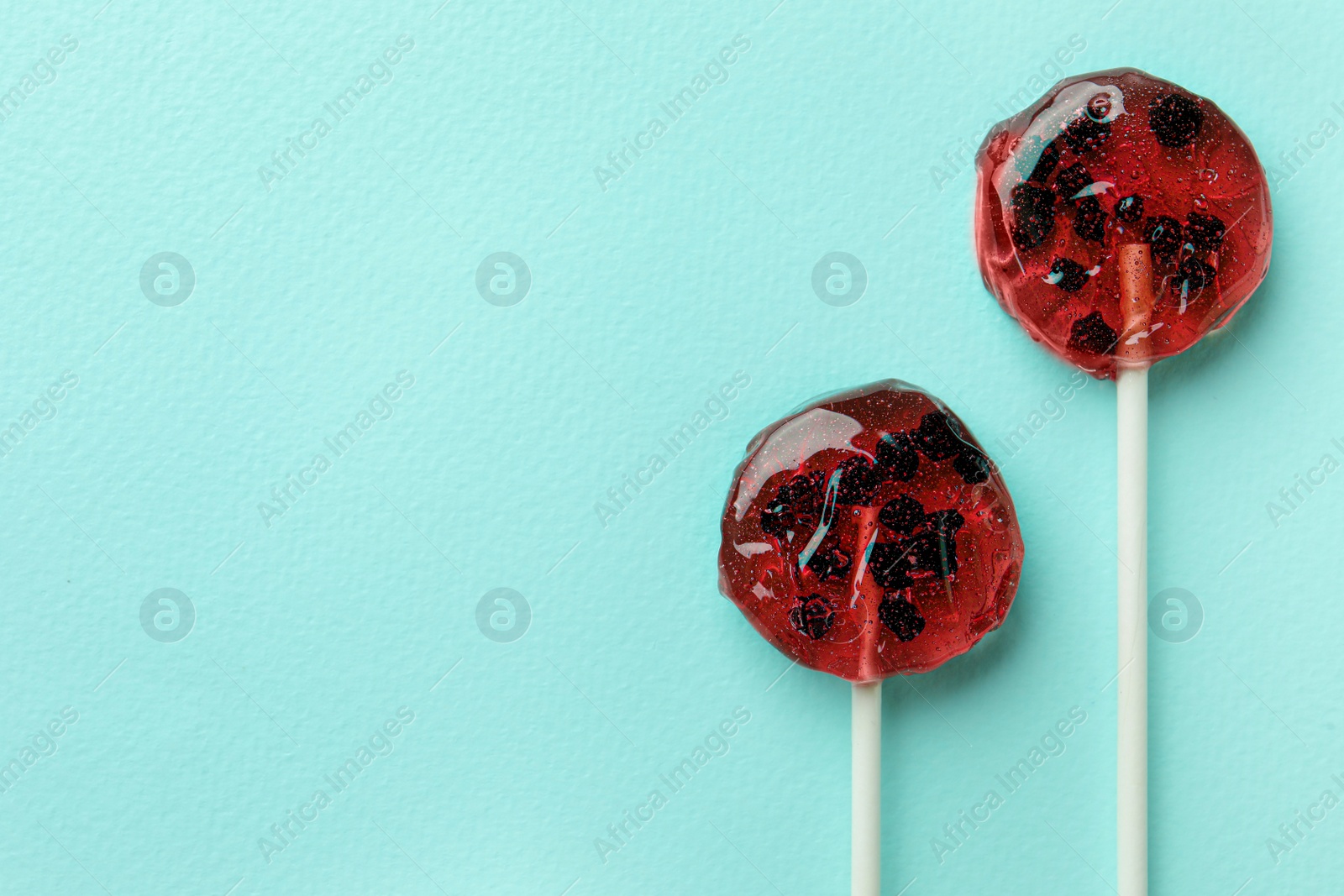 Photo of Sweet colorful lollipops with berries on turquoise background, flat lay. Space for text