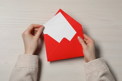 Woman taking card out of letter envelope at light wooden table, top view