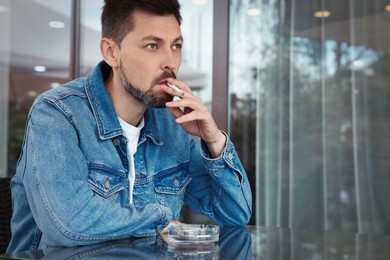 Photo of Handsome man smoking cigarette at table in outdoor cafe