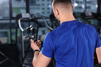 Photo of Man recording workout on camera at gym, back view. Online fitness trainer