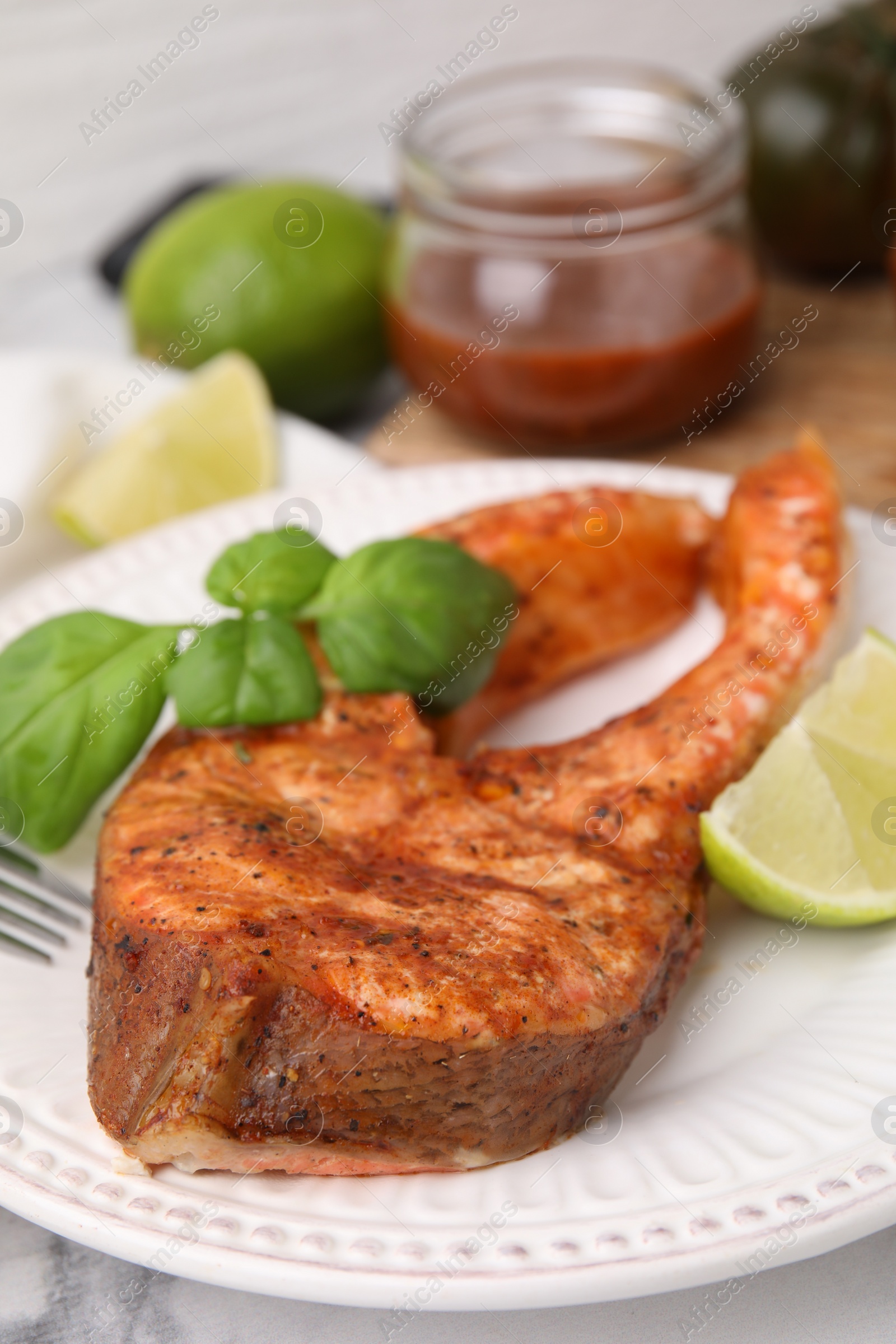 Photo of Freshly cooked fish, lime and basil on white marble table, closeup