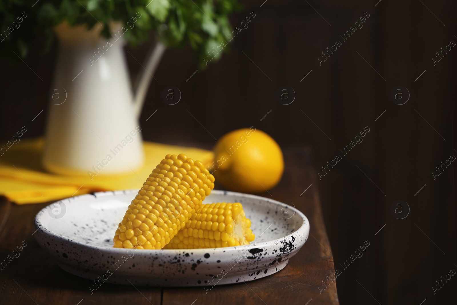 Photo of Plate with ripe corn cobs on table against dark background. Space for text