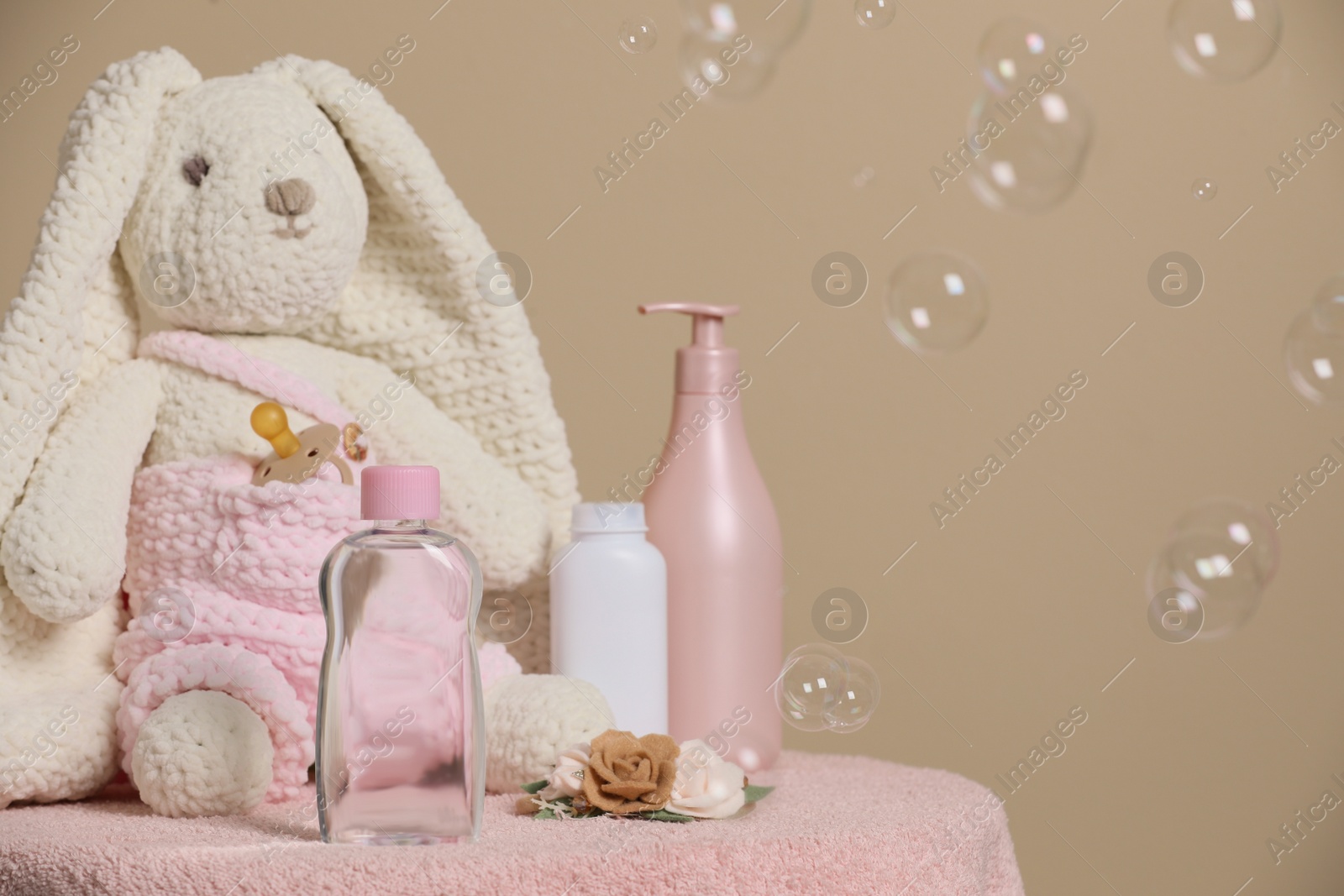 Photo of Baby cosmetic products, toy bunny, accessories and soap bubbles on beige background. Space for text
