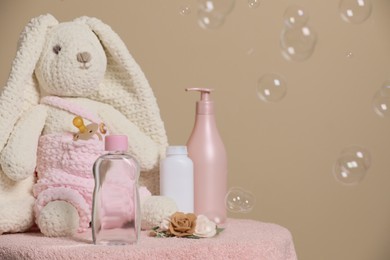 Baby cosmetic products, toy bunny, accessories and soap bubbles on beige background. Space for text