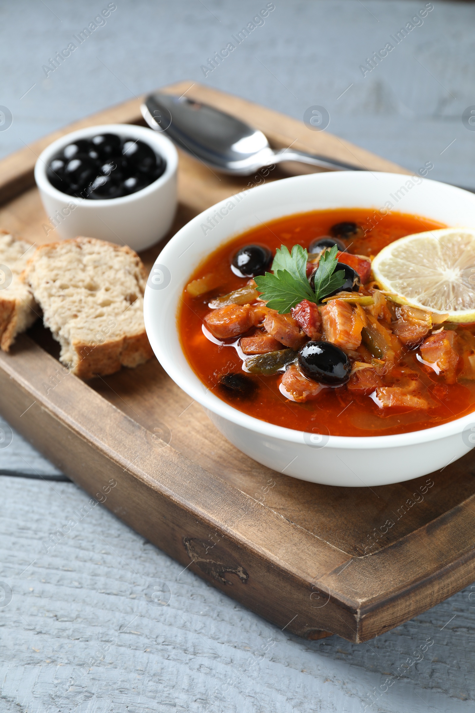 Photo of Meat solyanka soup with sausages, olives and vegetables in bowl served on grey wooden table, closeup