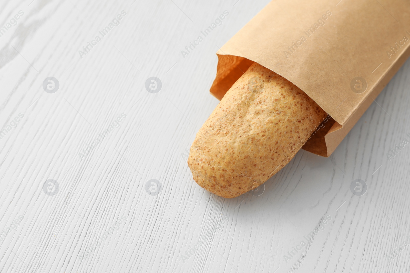 Photo of Baguette in paper bag on wooden table. Space for text