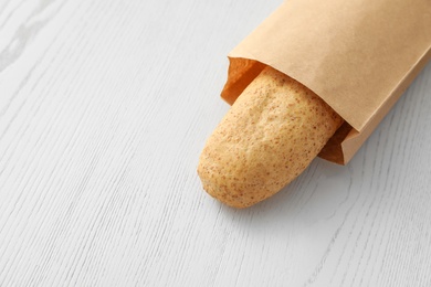 Photo of Baguette in paper bag on wooden table. Space for text