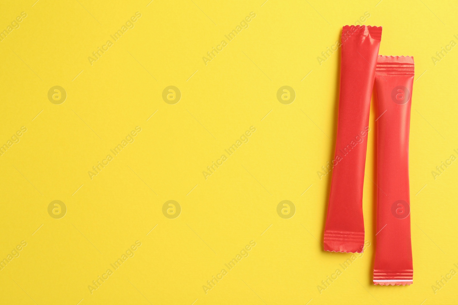 Photo of Red sticks of sugar on yellow background, flat lay. Space for text