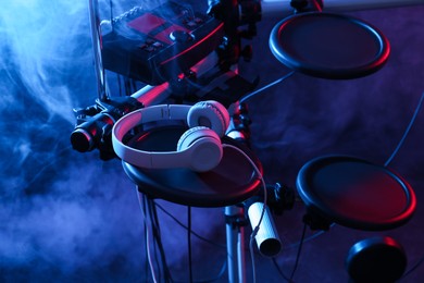Photo of Modern electronic drum kit with headphones on dark background, color toned. Musical instrument