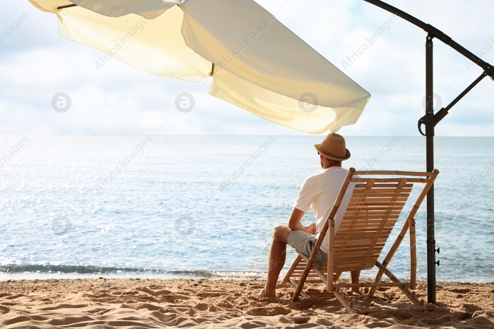 Photo of Man relaxing on deck chair at sandy beach. Summer vacation