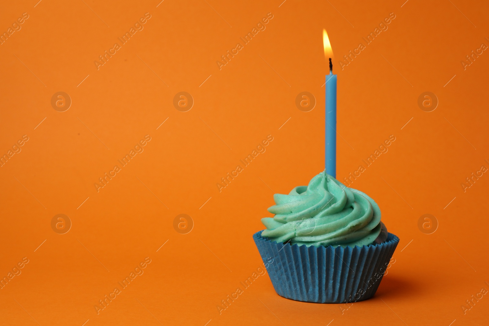 Photo of Delicious birthday cupcake with turquoise cream and burning candle on orange background. Space for text