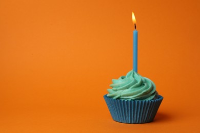 Photo of Delicious birthday cupcake with turquoise cream and burning candle on orange background. Space for text