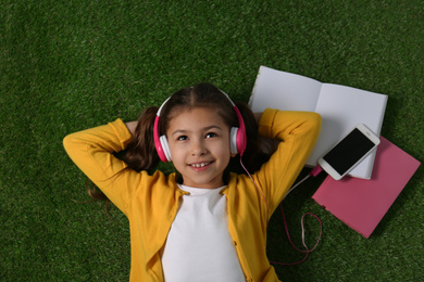 Photo of Cute little girl listening to audiobook on grass, top view