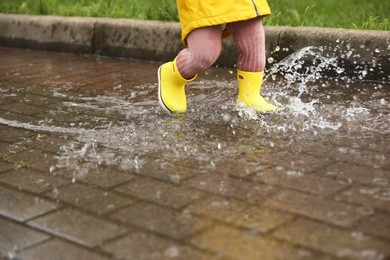 Girl walking in puddle outdoors on rainy weather, closeup