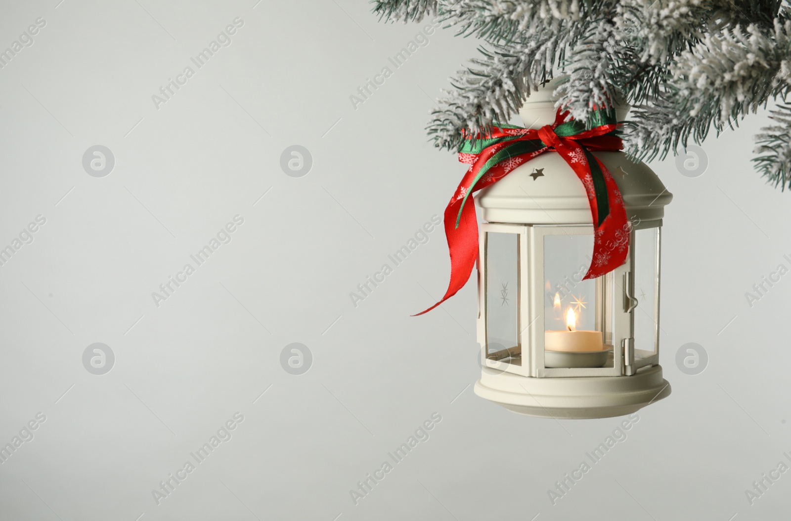 Photo of Christmas lantern with candle hanging on snowy fir tree branch against light background. Space for text