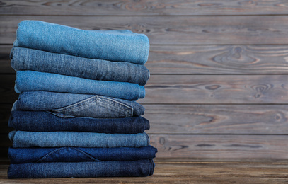 Photo of Stack of different jeans on wooden table. Space for text