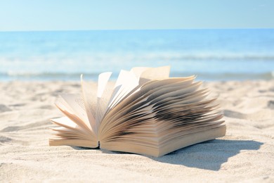 Open book on sandy beach near sea