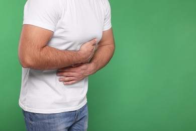 Photo of Man suffering from stomach pain on green background, closeup and space for text
