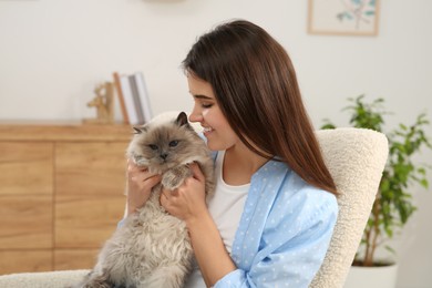 Woman with her cute cat on soft armchair at home