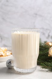 Photo of Glass of delicious eggnog and fir branch on light table, closeup