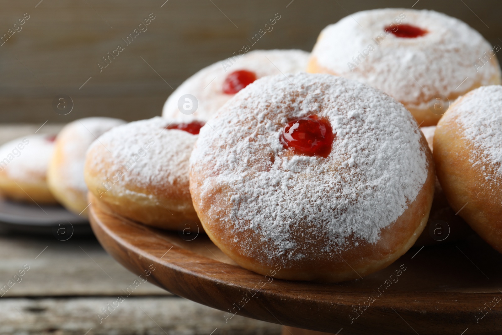 Photo of Delicious donuts with jelly and powdered sugar on wooden pastry stand, closeup