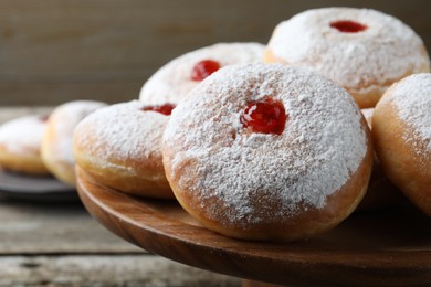 Delicious donuts with jelly and powdered sugar on wooden pastry stand, closeup