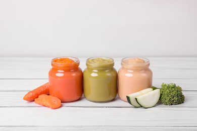 Photo of Jars of healthy baby food and vegetables on white wooden table