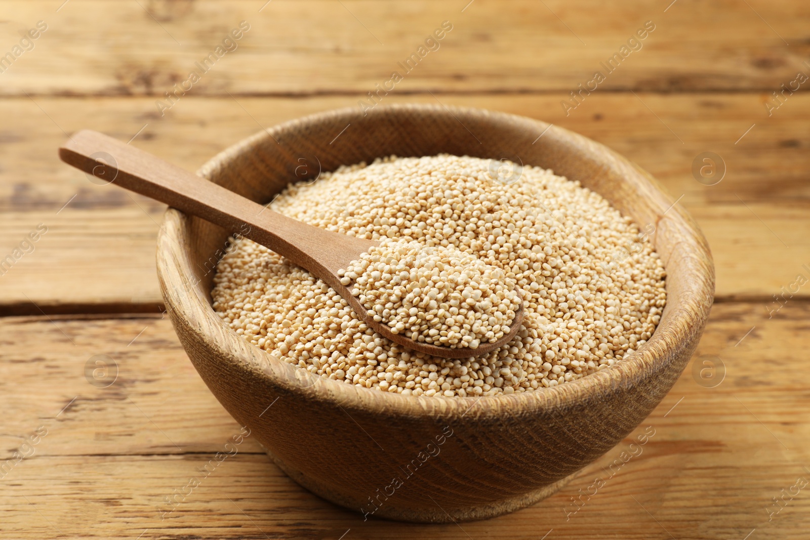 Photo of Dry quinoa seeds and spoon in bowl on wooden table, closeup