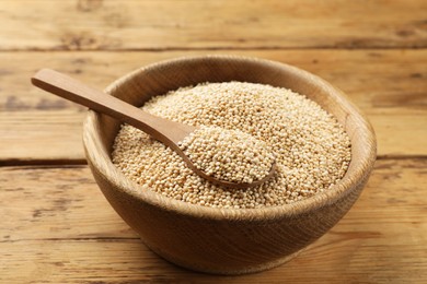 Photo of Dry quinoa seeds and spoon in bowl on wooden table, closeup