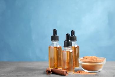 Photo of Bottles of essential oils, cinnamon sticks and powder on table against blue background