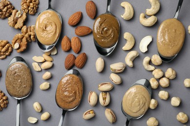 Photo of Tasty nut butters in spoons and raw nuts on gray table, flat lay