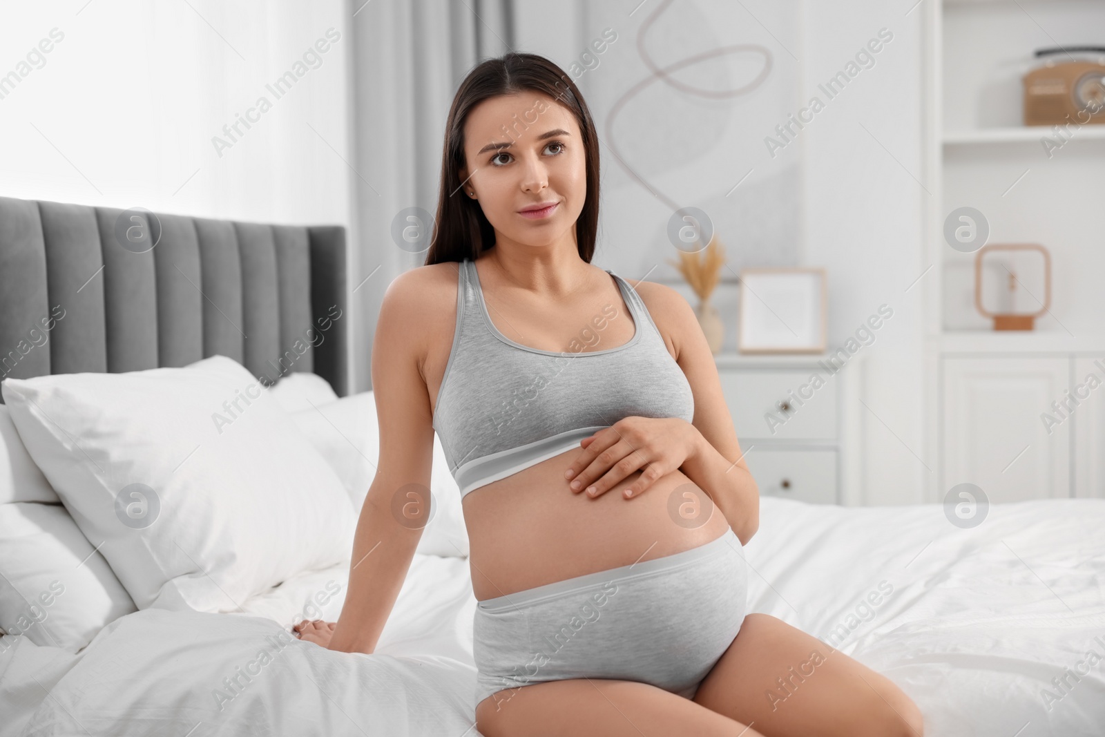 Photo of Beautiful pregnant woman in comfortable maternity underwear on bed at home