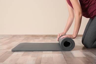 Woman rolling yoga mat on floor indoors, closeup. Space for text