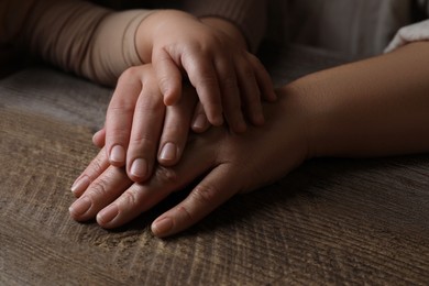 Photo of Family holding hands together at wooden table, closeup