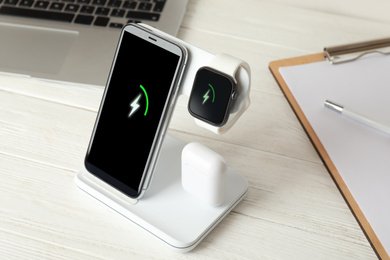 Set of gadgets charging with wireless device on white wooden table