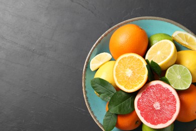 Photo of Different cut and whole citrus fruits on black table, top view. Space for text