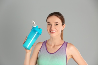 Photo of Athletic young woman with protein shake on light grey background
