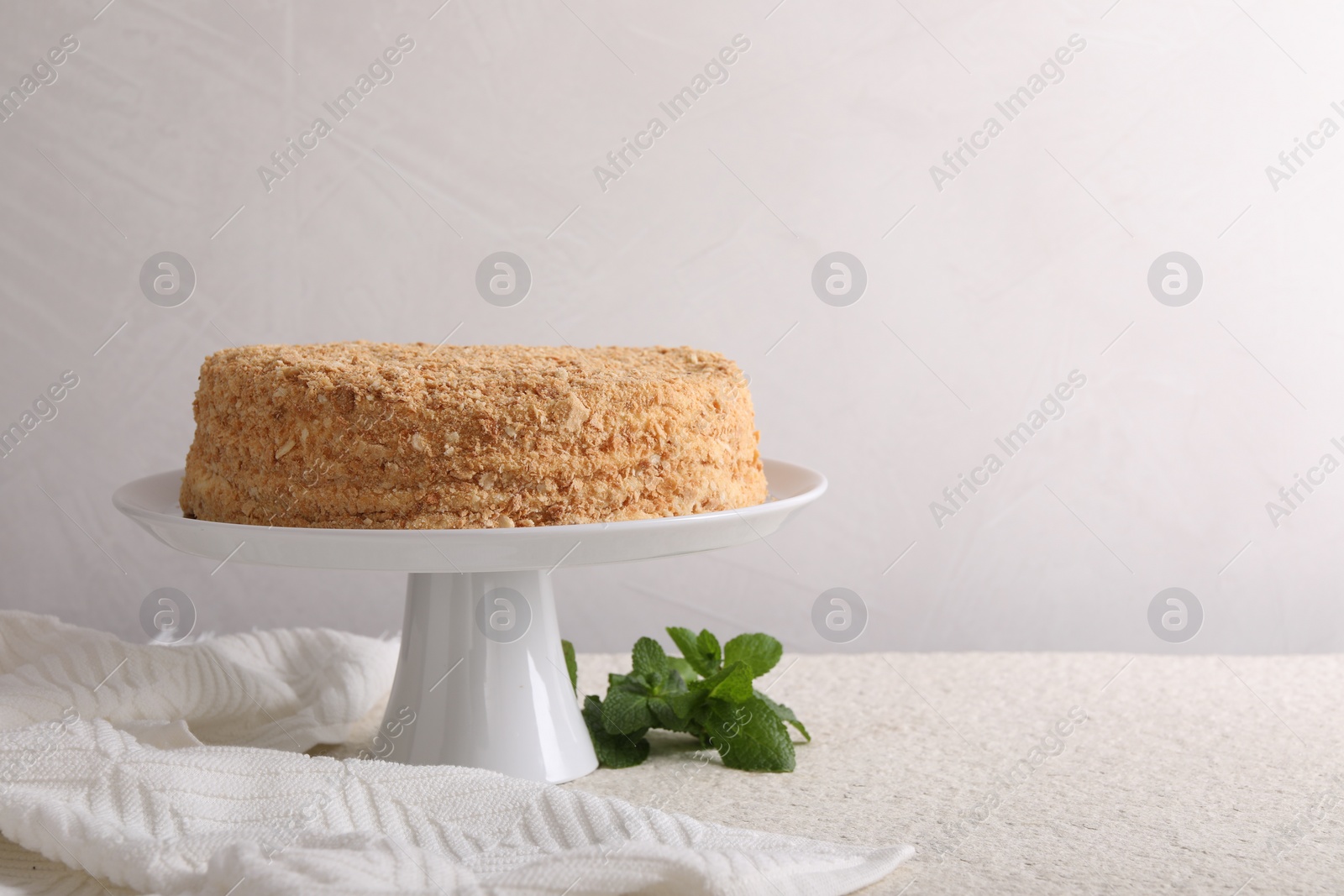 Photo of Delicious Napoleon cake and mint on beige table against light background, space for text