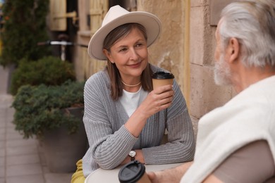 Affectionate senior couple sitting in outdoor cafe and drinking coffee, space for text