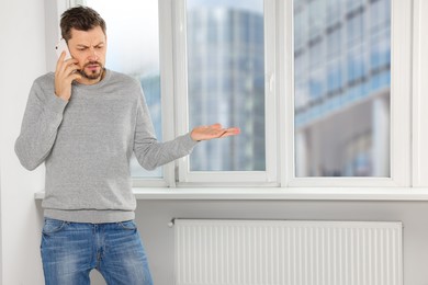 Man talking on phone near window indoors, space for text