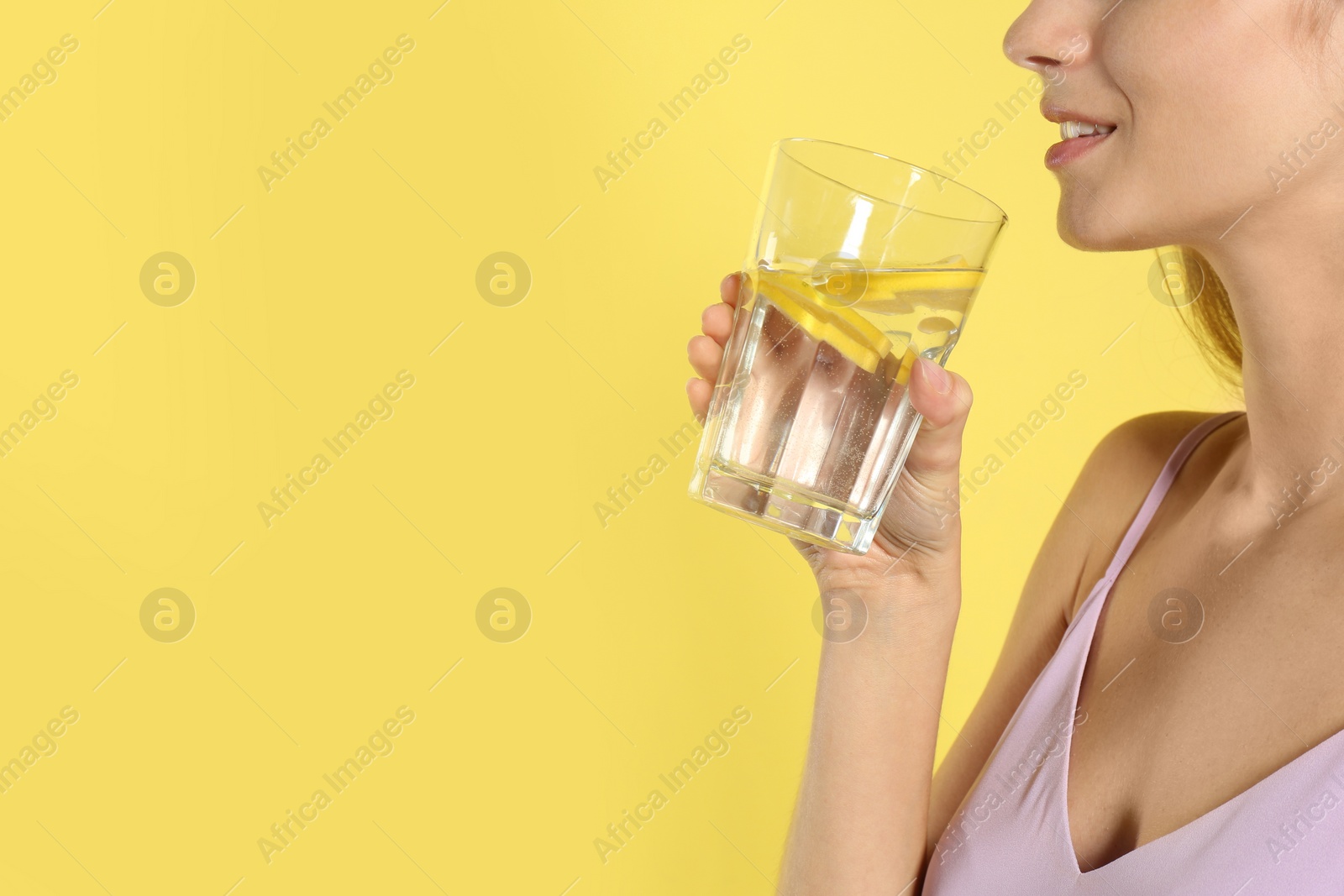 Photo of Young woman drinking lemon water on yellow background, closeup. Space for text