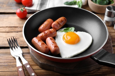 Photo of Romantic breakfast with fried sausages and heart shaped egg on wooden table. Valentine's day celebration
