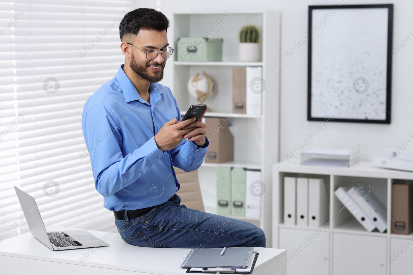 Photo of Handsome young man using smartphone in office, space for text